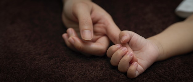 Neugeborene Babyhand, die Finger des Elternteils hält