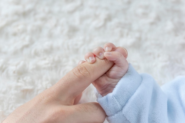 Neugeborene Babyhand, die Mutterfinger auf Bett hält