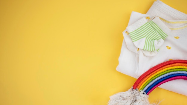 Neugeborene Babykleidung und DIY-Regenbogen auf gelbem Hintergrund Geburtstagskarte für die Babyparty