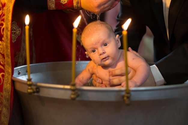 Neugeborene Taufe durch Wasser mit den Händen des Priesters