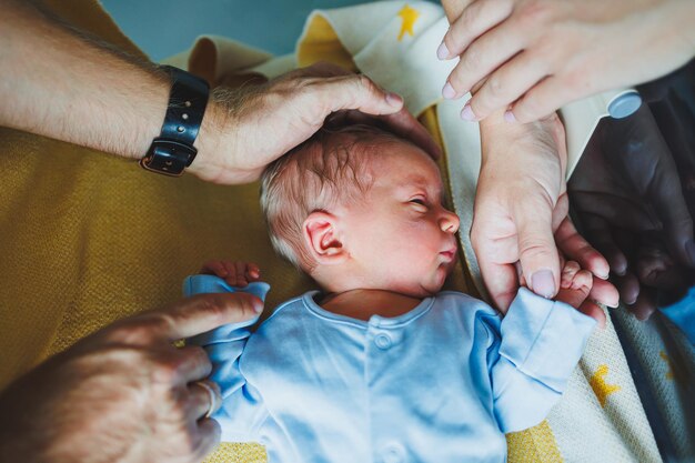 Neugeborener Junge in den Armen seiner Mutter und seines Vaters, der auf ihren Armen liegt. Nahaufnahme von oben. Junge Eltern halten ihr kleines Baby.