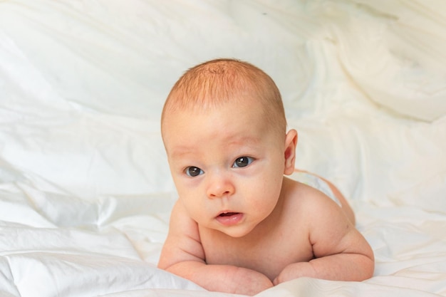 Neugeborenes Baby auf weißer Bettwäsche, das auf dem Bauch auf dem Bett liegt