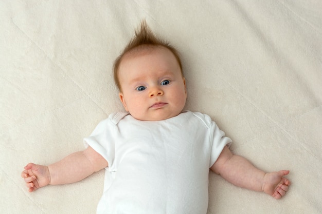 Neugeborenes Baby, das auf Bett im weißen Schlafanzug liegt.