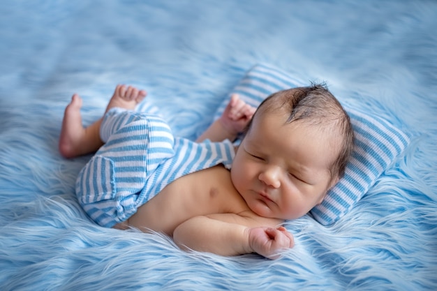 Neugeborenes Baby, das auf blauem Fell schläft und einen Matrosenanzug mit einer modischen Frisur trägt