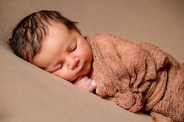 Neugeborenes Baby, das friedlich mit kariertem Stoff auf braunem Hintergrund schläft.