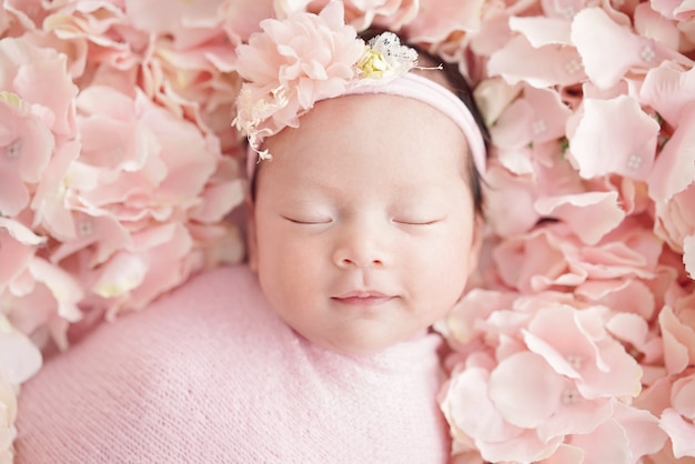 Neugeborenes Baby hat einen süßen Traum mit einem süßen Lächeln mit einem rosa Blumenstirnband und rosa Windeln Kleines Mädchen, das auf rosa Hortensien schläft Nahaufnahmeaufnahme
