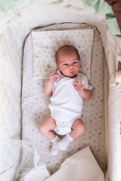Neugeborenes Baby im Bett. Neugeborenes Kind im weißen Bodykit in heller Wiege liegend.