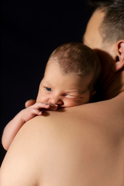 neugeborenes Baby in den Armen des Vaters auf schwarzem Hintergrund