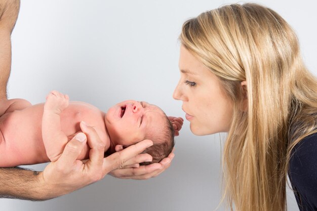 Neugeborenes Baby in den Händen des Vaters. Die Hände eines Vaters halten sein kleines Kind. Blonde Mutter küsst Baby