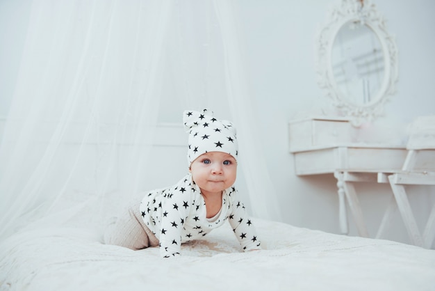 Neugeborenes Baby in einem weißen Anzug und schwarzen Sternen ist ein weißes weiches Bett im Studio