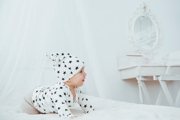 Neugeborenes Baby in einem weißen Anzug und schwarzen Sternen ist ein weißes weiches Bett im Studio