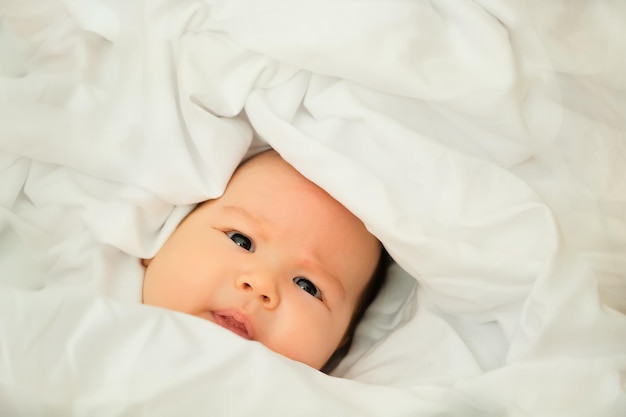 Neugeborenes Baby lächelt und lacht zeigt Emotionen Baby liegt auf einem weißen Tuch