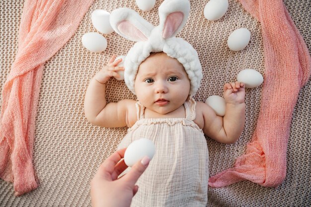 Neugeborenes Baby liegt auf einem Bett in pastellfarbenen Farben wie ein Osterhase auf dem Gras mit Eiern