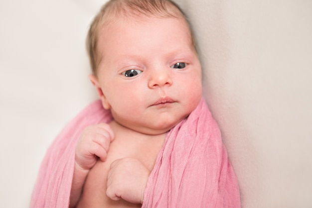 Neugeborenes Baby schaut in einer rosa Decke nach unten