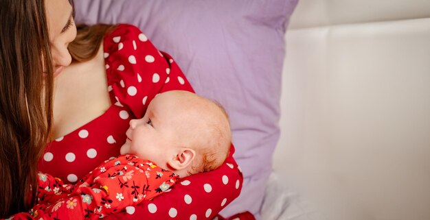 Neugeborenes Mädchen in rotem Polka-Dot-Kleid auf den Händen der Mutter