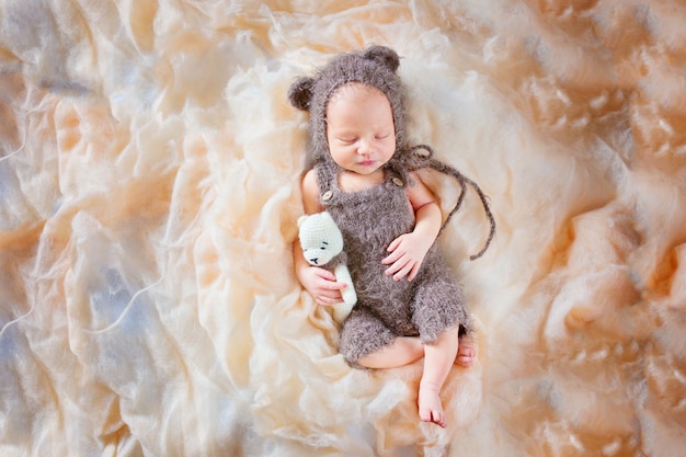 Neugeborenes schlafendes Baby in einem Bärenkostüm und mit einem Spielzeug. Schönes Posing eines neugeborenen Babys in einem Hut mit Ohren und Overall.