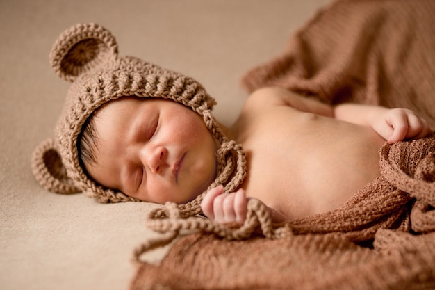 Neugeborenes schlafendes Baby in Strickmütze liegt auf braunem Stoff.