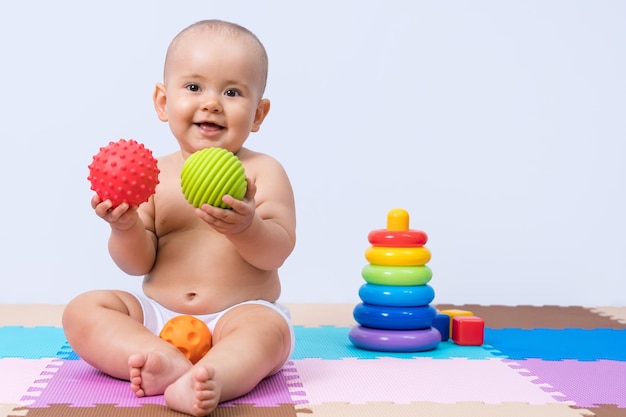 Neugeborenes sitzt auf dem Boden und spielt mit einem grünen und roten Gummiball