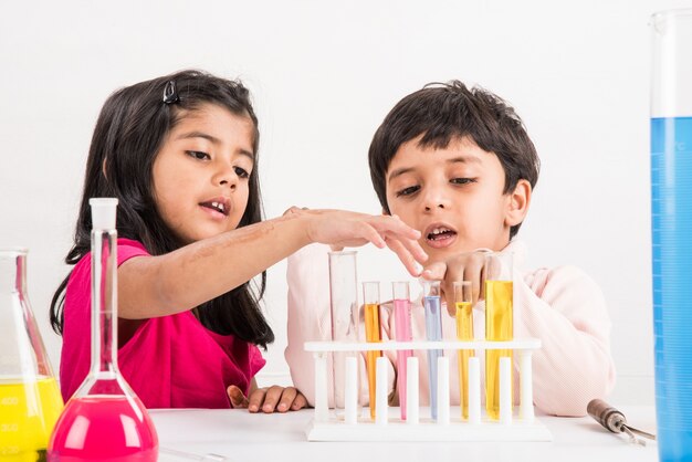 Neugierige kleine indische Schulkinder oder Wissenschaftler, die Naturwissenschaften studieren, mit Chemikalien oder Mikroskopen im Labor experimentieren, selektiver Fokus