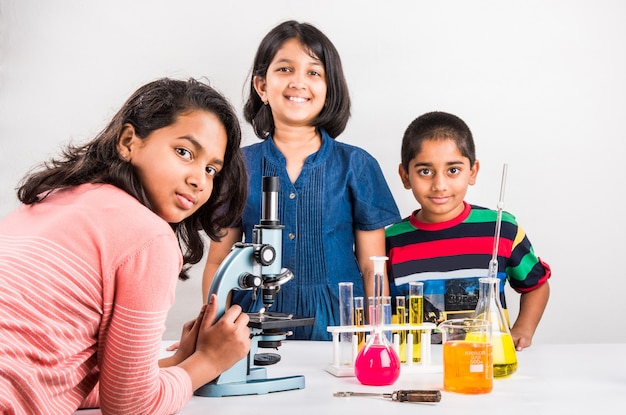 Neugierige kleine indische Schulkinder oder Wissenschaftler, die Naturwissenschaften studieren, mit Chemikalien oder Mikroskopen im Labor experimentieren, selektiver Fokus