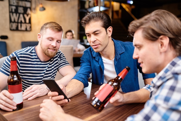 Neugierige Männer lesen Nachrichten am Telefon, während sie zusammen Bier trinken