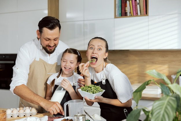 Neugierige Mutter, die sich die Kamera anschaut und den Mund öffnet, der Rucola isst Glückliche Tochter, die Milch in den Armen hält