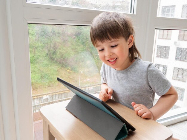 Foto neugieriger junge schaut sich zeichentrickfilme auf einem digitalen tablet an. kind benutzt ein elektronisches gerät, um über das internet zu telefonieren