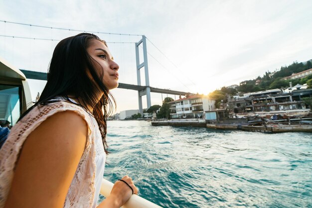 Neugieriges junges Mädchen betrachtet die Stadt überrascht, Bootsfahrt auf dem Bosporus, moderne Brücke