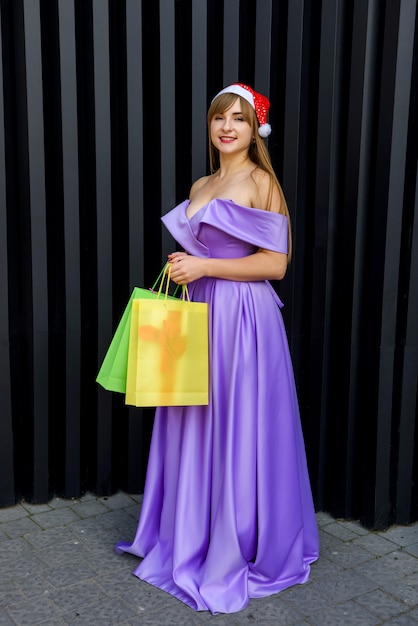 Neujahr Feierlichkeiten. Glückliche Frau im modischen Abendkleid mit bunten Geschenktüten in Weihnachtsmütze