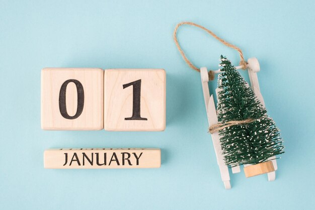 Neujahr ist hier Konzept. Oben oben Foto mit Draufsicht von Holzwürfeln, die den ersten Tag des Jahres und einen kleinen Weihnachtsbaum auf einem Schlitten zeigen, isoliert auf hellblauem Hintergrund