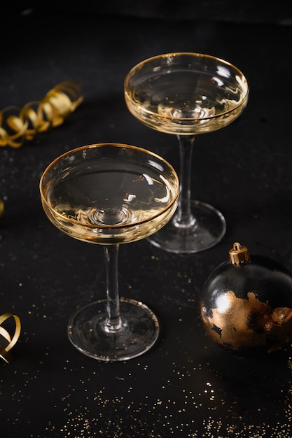 Neujahrs-Champagnergläser und weihnachtliche Golddekorationen auf schwarzem Hintergrund