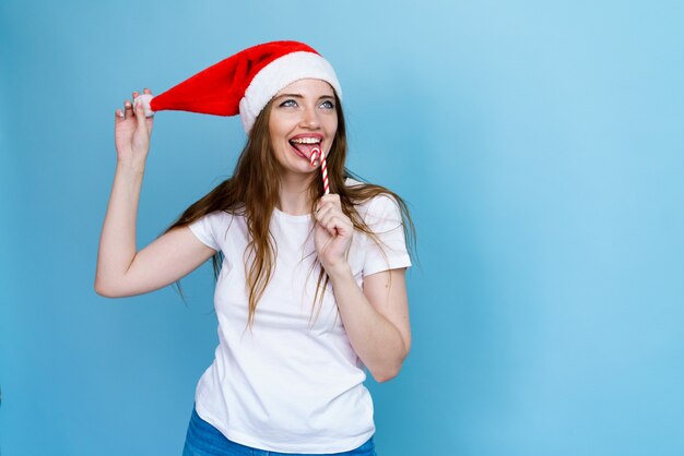 Neujahrs- und Weihnachtsferienkonzept lächelnde junge Frau in Weihnachtsmann-Hut mit Lutscher auf blauem...