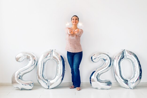 Neujahrsfeier und Partykonzept - Glückliche junge Frau mit Wunderkerzen nahe silbernen 2020 Luftballons.
