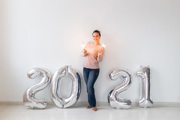 Neujahrsfeier und Partykonzept - Glückliche junge Frau mit Wunderkerzen nahe silbernen Luftballons 2021