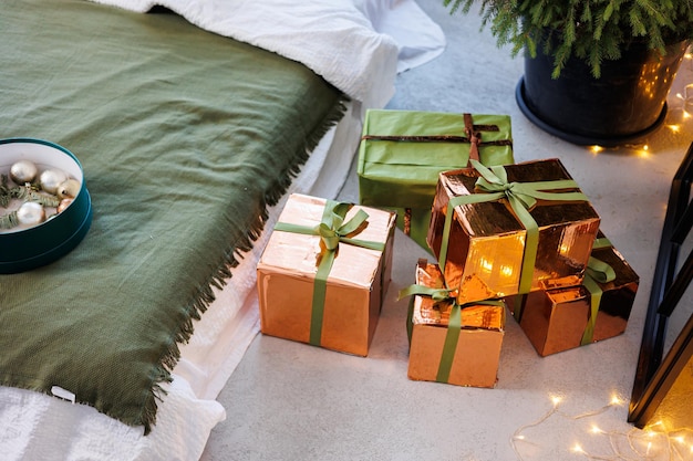 Neujahrsgeschenke in Papier und bunten Bändern unter dem Weihnachtsbaum auf dem Boden an Silvester Ein mit Spielzeug geschmückter Weihnachtsbaum steht neben dem Bett