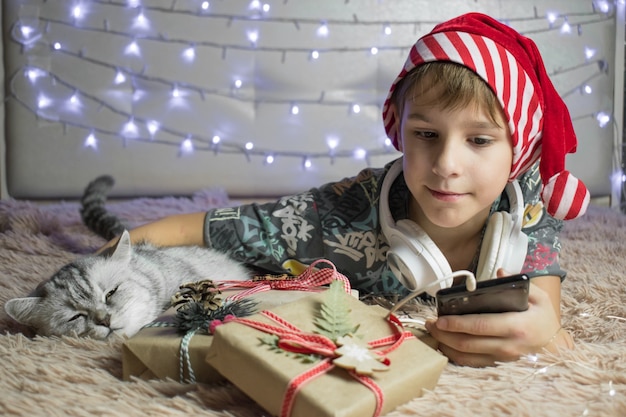 Neujahrsgrüße online. Der Junge liegt mit einer Katze und Geschenken auf dem Bett.