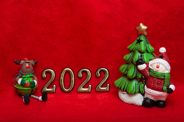 Neujahrskonzept brauner Hirsch, Schneemann mit Tannenbaum und goldenen Zahlen auf rotem Grund. Das neue Jahr 2022 kommt bald. Postkartenlayout, Verpackung. Banner