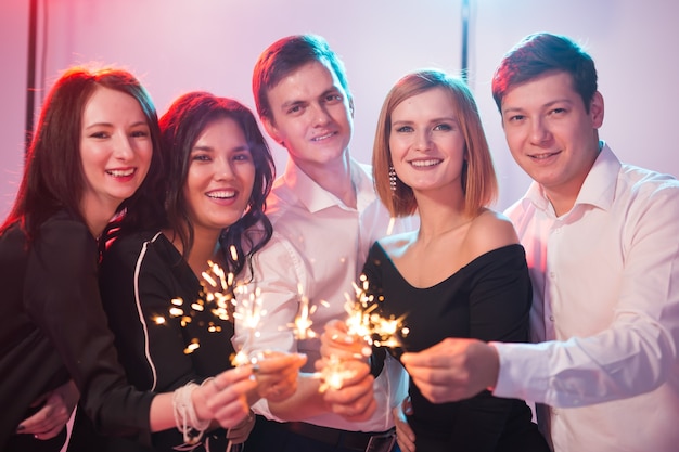 Neujahrsparty, Feier und Feiertagskonzept - Junge fröhliche Männer und Frauen, die brennende Wunderkerzen halten