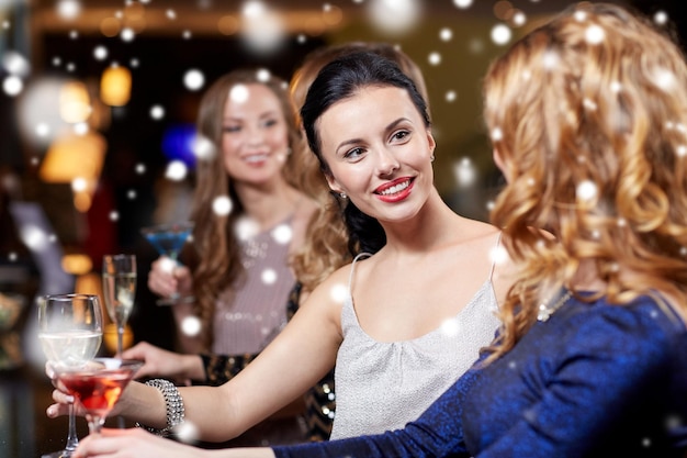 Neujahrsparty, Weihnachten, Winterferien und Menschenkonzept – glückliche Frauen trinken Champagner und Cocktails im Nachtclub über Schnee