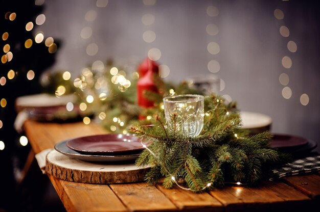 Neujahrstisch für ein festliches Abendessen serviert. Weihnachtseinstellung auf Holztisch mit Dekorationstafeln und Weingläsern und roten Kerzen auf grauem verschwommenem Bokehhintergrund