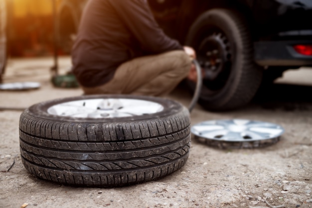 Neumático nuevo tirado en el pavimento cerca del mecánico listo para reemplazar el de un automóvil.