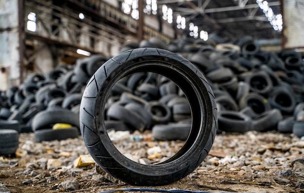 El neumático viejo y sucio está en el suelo junto a los otros neumáticos usados en la planta dañada Basura de goma del automóvil Primer plano
