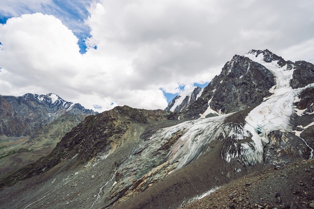 Nevado cordillera gigante bajo cielo nublado. Cresta rocosa con nieve. Enorme glaciar. Ladera helada con corrientes de agua. Maravillosas montañas Atmosférico minimalista paisaje montañoso de la naturaleza.