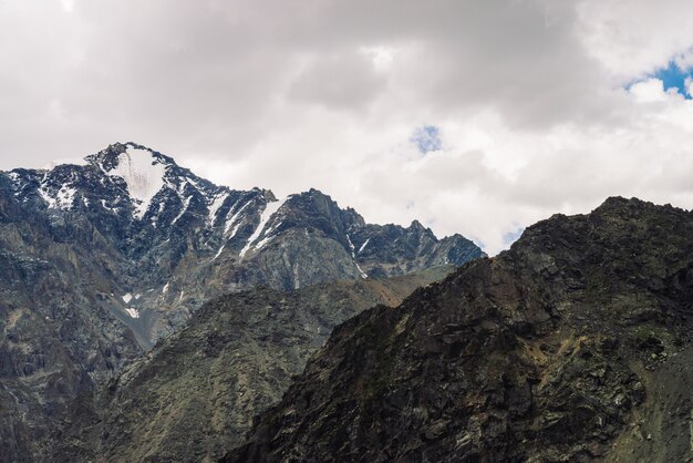 Neve no cume rochoso gigante sob céu nublado. Montanha atmosférica escura. Incrível cordilheira nevada em tempo nublado. Pedras maravilhosas. Maravilhosa paisagem sombreada de natureza majestosa das terras altas