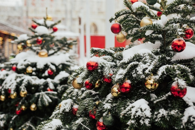 Neve nos galhos das árvores de Natal decoradas com bolas vermelhas e douradas nas ruas da cidade. Mercado de Natal.