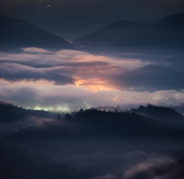 Nevoeiro misterioso na colina com cidade iluminada no vale ao amanhecer no parque nacional