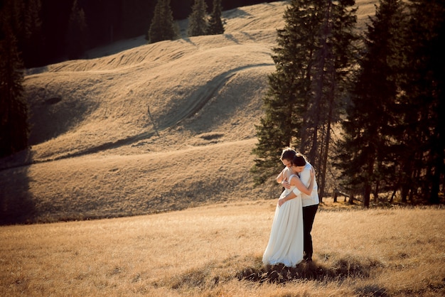 Newlyweds umarmte in einem feld mit kiefern