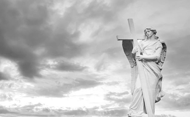 Ángel de lápida con alas y cruz sobre fondo de cielo