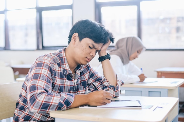 Ängstlicher männlicher asiatischer Student sitzt für eine Prüfung in der Schulklasse