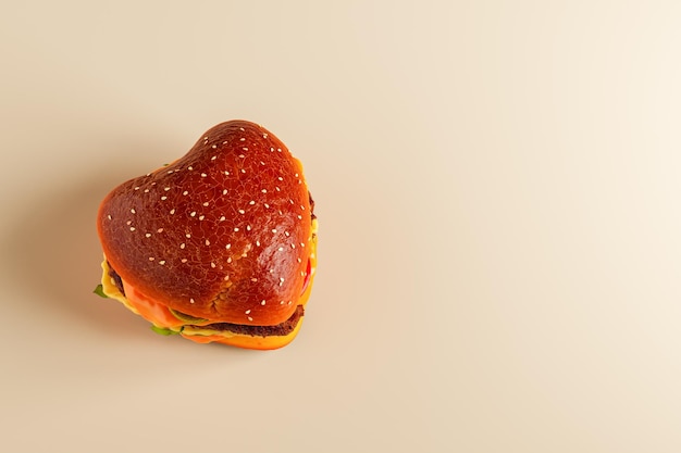 Ángulo alto de hamburguesa apetitosa en forma de corazón con rebanadas de verduras verdes frescas en fondo beige